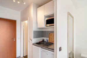 A compact kitchen with a microwave, sink, and a cutting board.