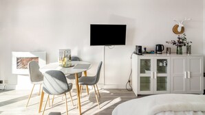 A modern room with a white dining table, grey chairs, a flat-screen TV, a cabinet with glass doors, and a mounted deer head.