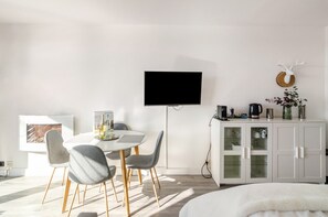 A modern room with a white dining table, grey chairs, a flat-screen TV, a cabinet with glass doors, and a mounted deer head.