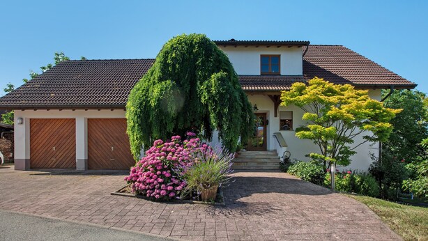 A house with a brick driveway, a garage, and a well-maintained garden with various plants and flowers. - Apartment 'Nussbäumle' with Private Terrace, Shared Garden and Wi-Fi (Rheinfelden (Baden))