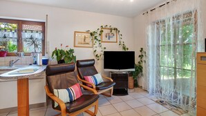 A living room with a TV, two leather chairs with cushions, a coffee table, a TV stand, and a large window with curtains. - Apartment 'Nussbäumle' with Private Terrace, Shared Garden and Wi-Fi (Rheinfelden (Baden))