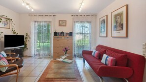 A living room with a red sofa, a TV, a wooden cabinet, and two windows with curtains. - Apartment 'Nussbäumle' with Private Terrace, Shared Garden and Wi-Fi (Rheinfelden (Baden))