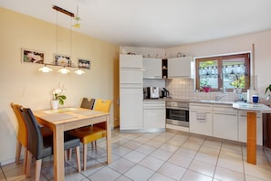 Une cuisine moderne avec des meubles blancs, une table à manger avec des chaises et une fenêtre donnant sur un paysage verdoyant.