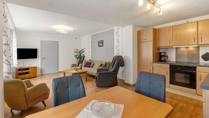 Een moderne woonkamer met een bank, fauteuils, een televisie en een eettafel.