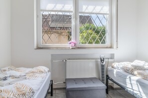 A room with two beds, a radiator, and a window with a view of buildings and trees.