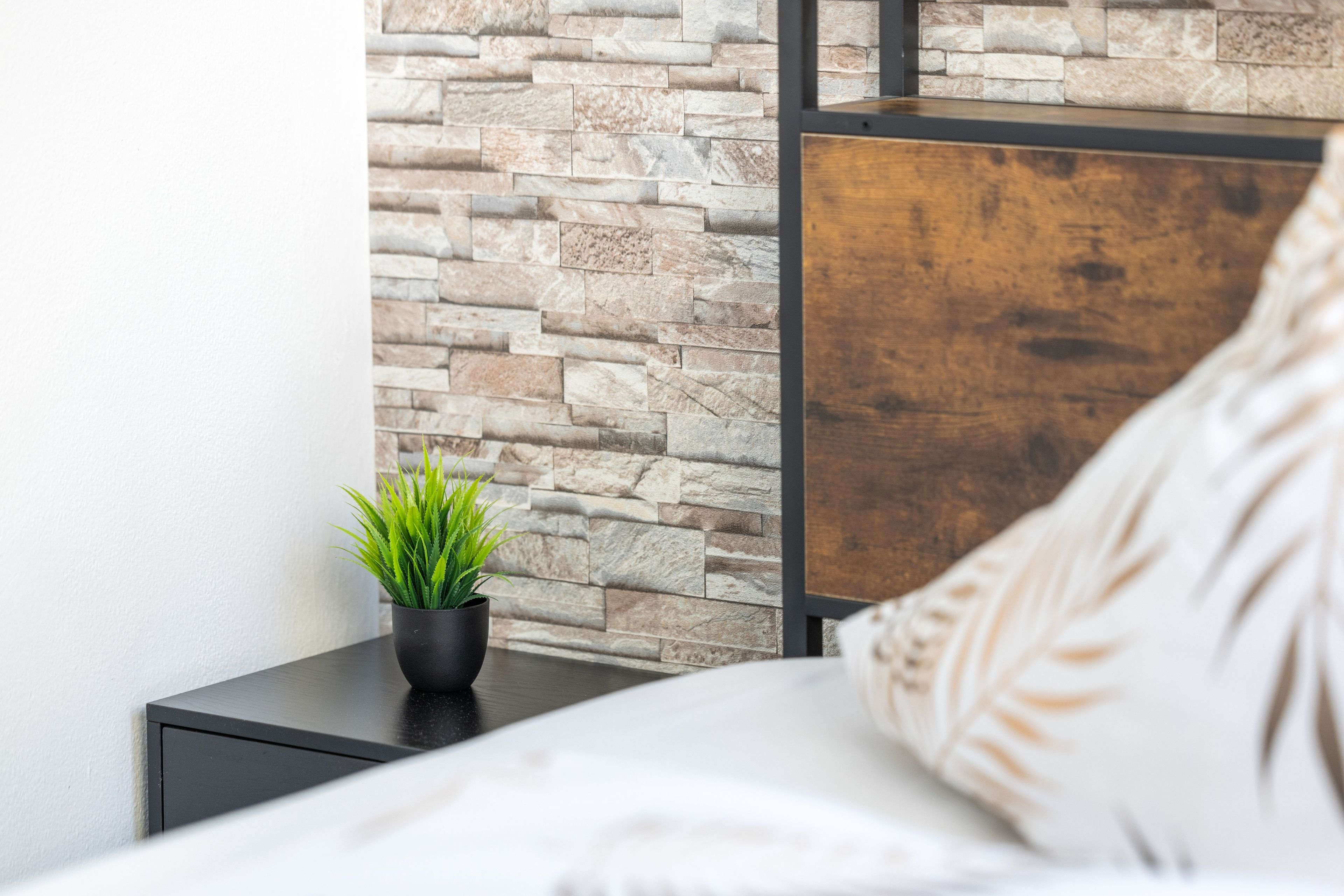 A bed with a headboard, a nightstand with a potted plant, and a stone wall.