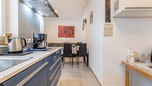 Cozinha compacta com eletrodomésticos modernos, sala de jantar com mesa e cadeiras, e calendário fixado na parede.