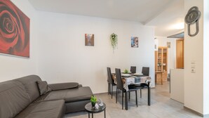 Uma sala de estar moderna com um sofá, uma mesa de jantar com cadeiras e uma pequena mesinha de apoio com uma planta.
