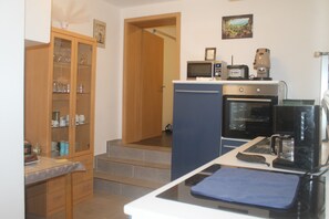 A compact kitchen with a microwave, coffee maker, and oven. There is a cabinet with glass doors and a small countertop.