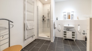 Casa de banho moderna com cabine de chuveiro em vidro, lavatório branco e porta-toalhas.