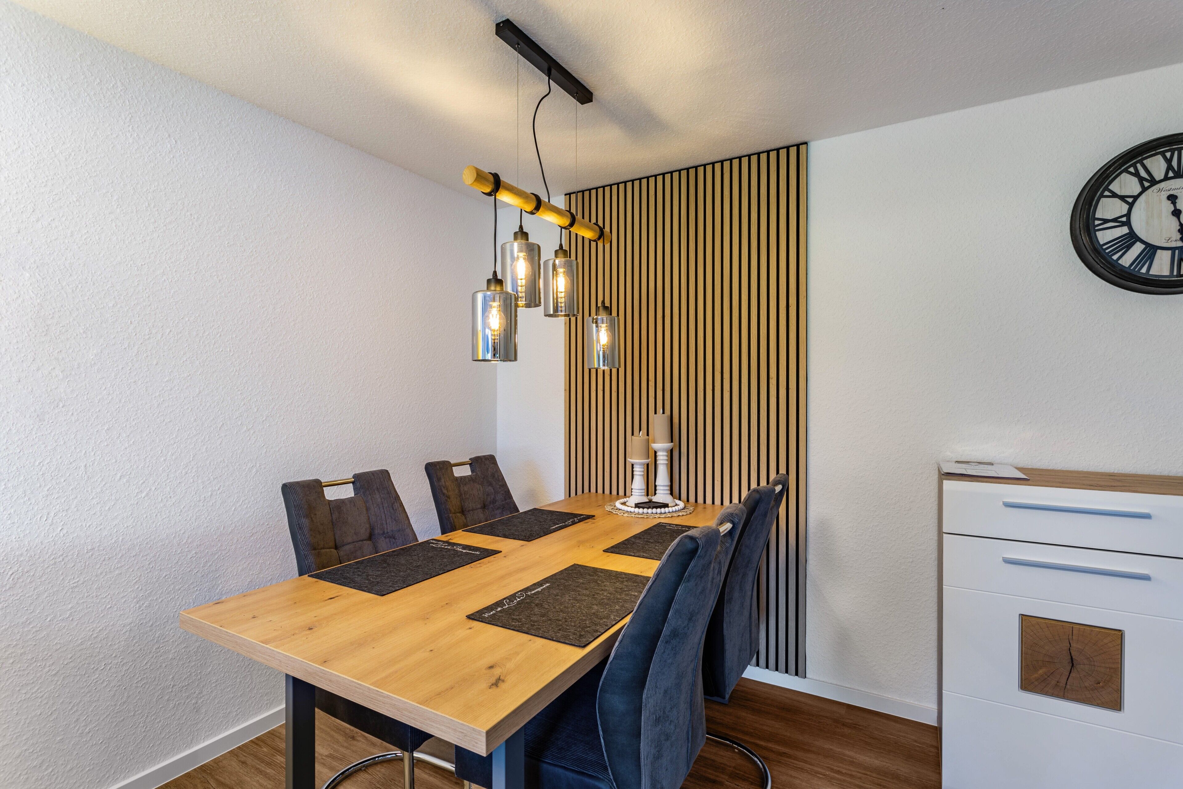 Een eethoek met een houten tafel, stoelen, een klok en een kast.