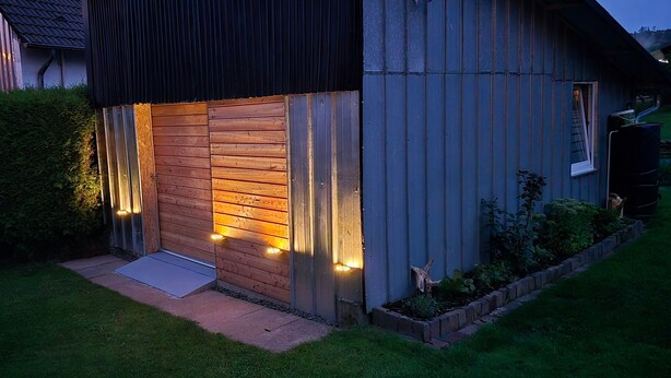 A house with a wooden door, a metal exterior, and a small porch with lights.