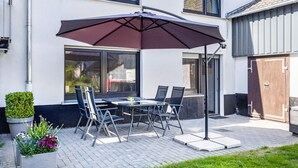 An outdoor patio with a table and chairs, a large umbrella, and a potted plant.