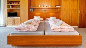 Un lit double avec un cadre en bois, un téléviseur posé sur un meuble et une bibliothèque contenant des livres et des objets décoratifs.