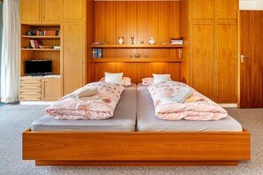 A double bed with a wooden frame, a television on a stand, and a bookshelf with books and decorative items.