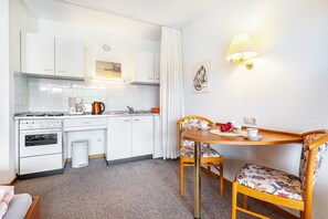 A compact kitchen with white cabinets, a stove, and a sink. There is a dining table with chairs and a wall-mounted lamp. - Studio '146' with Shared Garden and Wi-Fi (Bad Herrenalb)