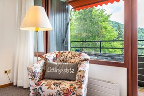 A floral-patterned armchair with a cushion labeled 'Lieblingsplatz' in a room with a window overlooking a forested area.