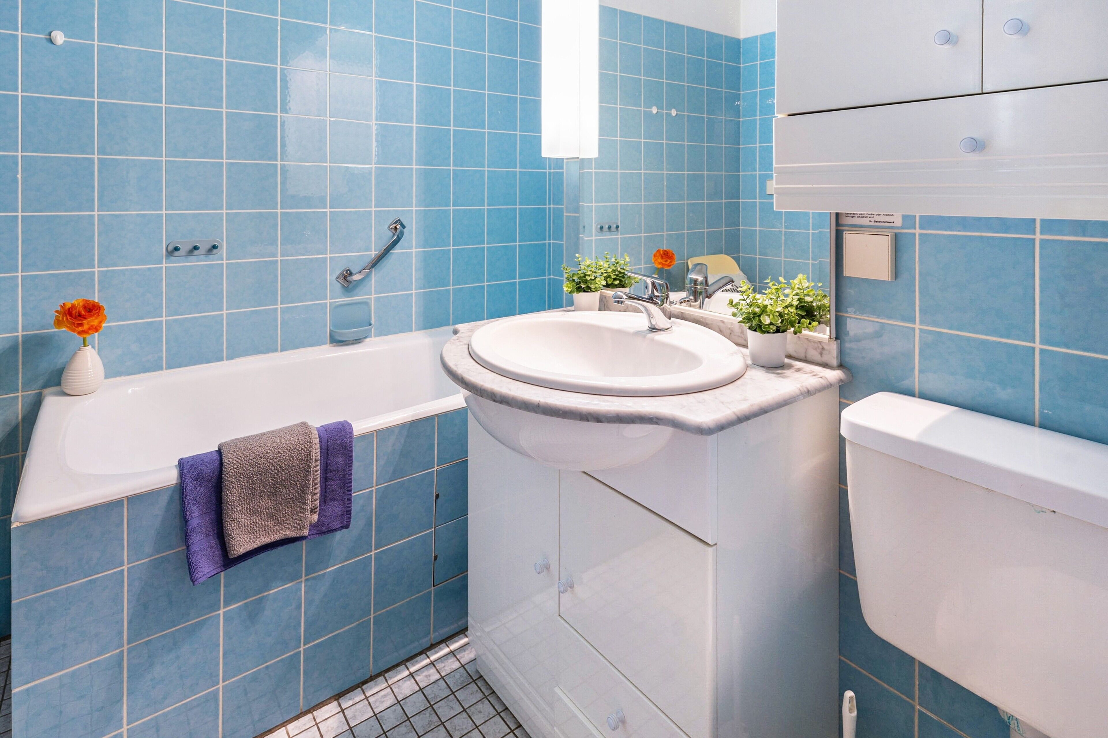 A bathroom with blue tiles, a bathtub, a sink, and a toilet.