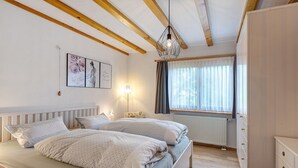 A bedroom with two beds, a radiator, a window with curtains, and a hanging light fixture.