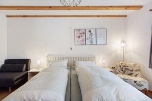 Quarto com duas camas, uma cadeira, um abajur e uma parede decorada com quadros.