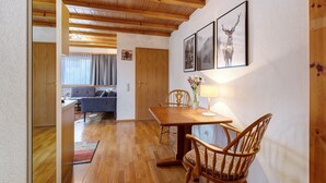 A dining area with a wooden table and chairs, a lamp, and framed pictures on the wall.