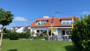 Una casa residencial con techo de tejas rojas, antena parabólica y césped cuidado.
