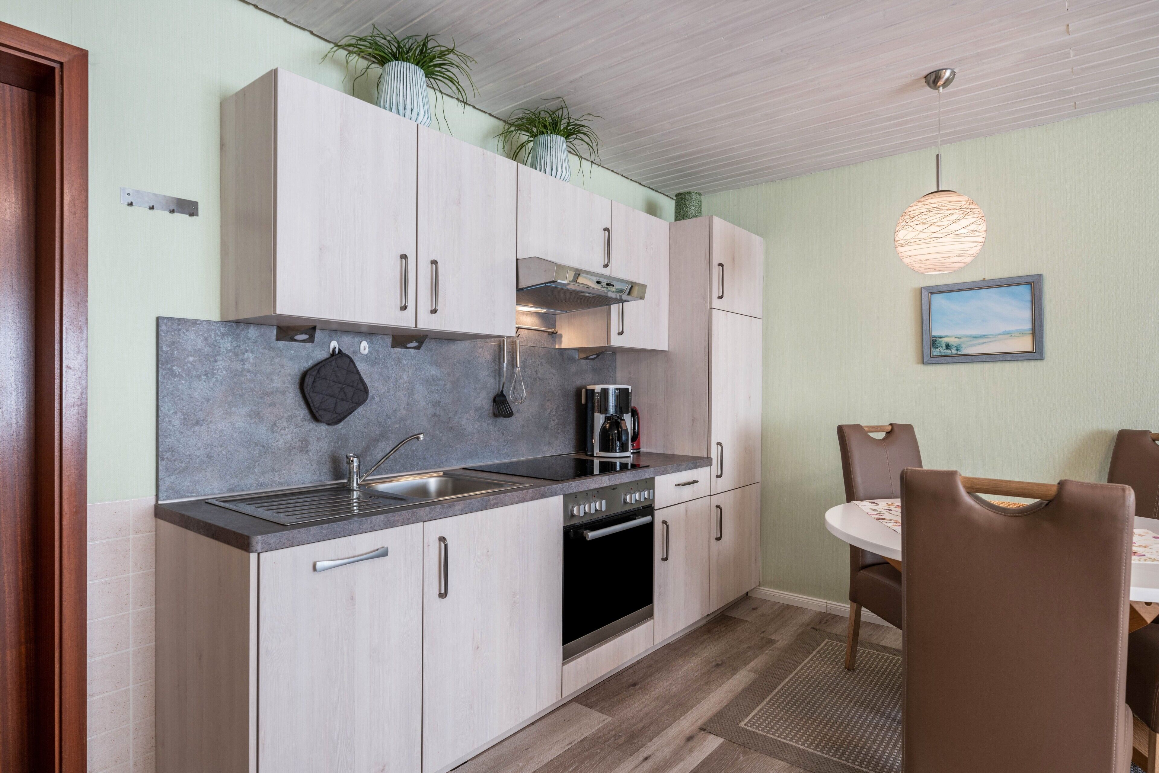 A kitchen with light wood cabinets, a stainless steel sink, and a coffee maker.