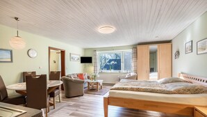 A room with a bed, a dining table, a sofa, a TV, and a window with curtains. - Apartment 'Luv Und Lee' with Private Terrace, Shared Garden and Wi-Fi (Schülp)