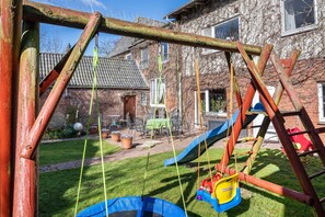Un conjunto de juegos de madera con un columpio, un tobogán, un trampolín y una casita en un patio trasero.