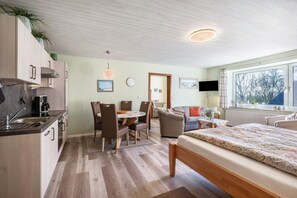 Una cocina moderna con armarios de madera, un comedor con sillas, una cama con cubrecama estampado y un ventanal con vistas.