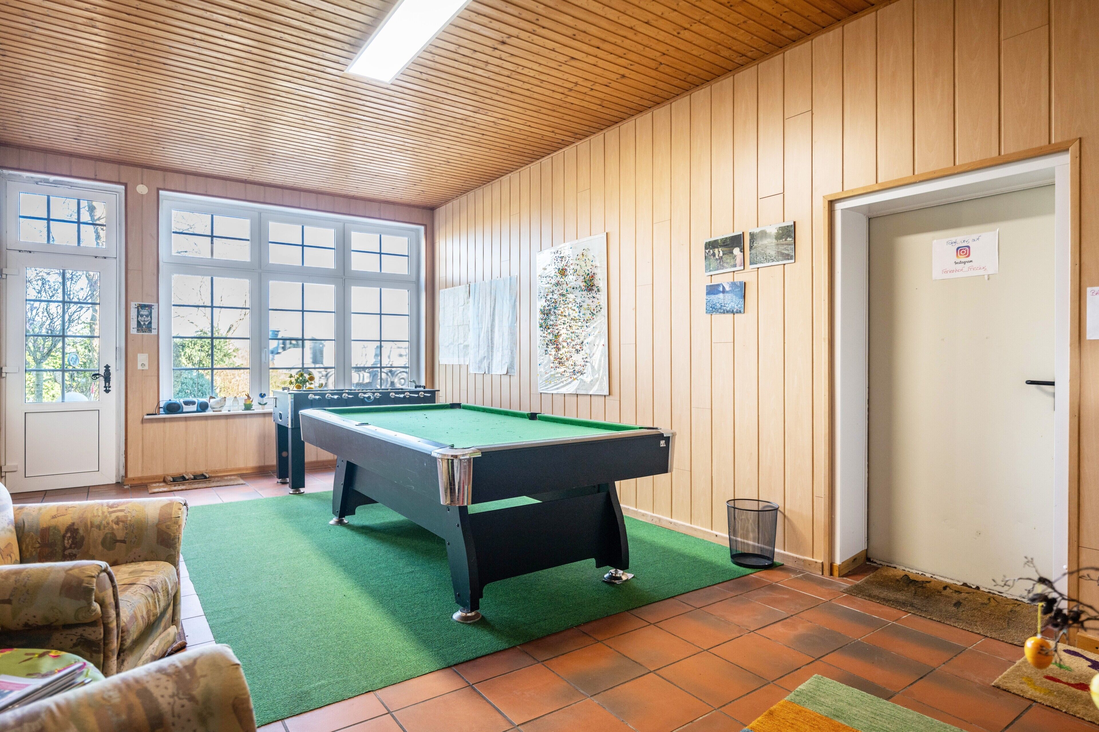 A pool table in a room with wooden walls, a green carpet, and a door with a sign.