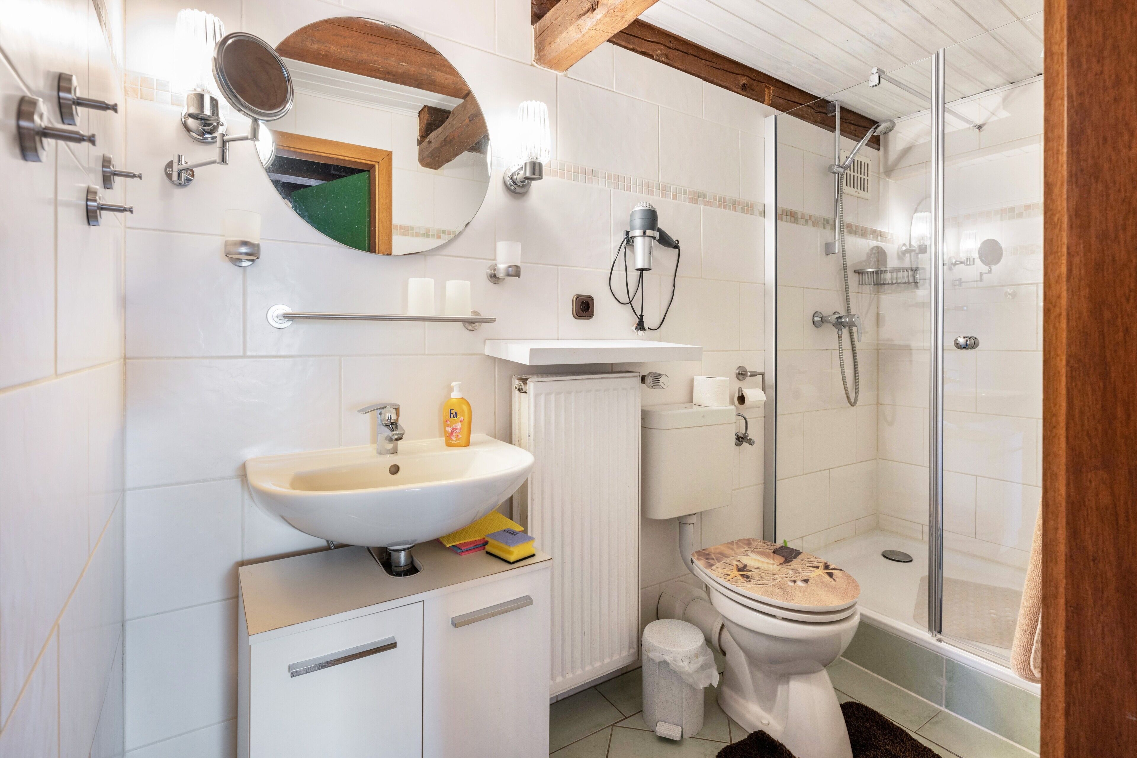 A bathroom with a sink, mirror, toilet, shower, and a radiator.