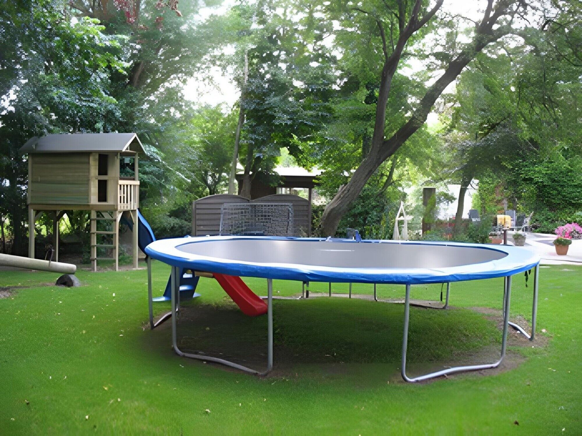 A trampoline in a grassy backyard with a slide and a wooden playhouse.