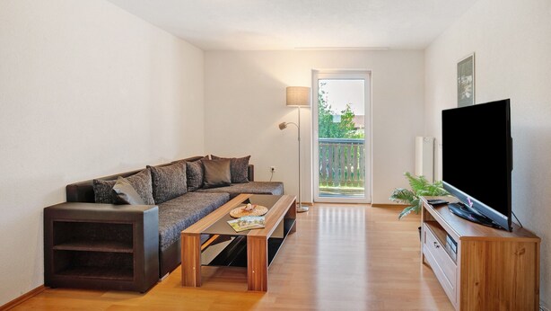 A living room with a sofa, a coffee table, a TV on a wooden stand, and a door leading to a balcony. - Apartment '1' with Balcony and Wi-Fi (Heroldstatt)