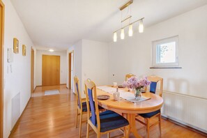 Un área de comedor con una mesa redonda, sillas, un florero con flores, una ventana y una puerta al fondo.