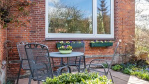 Eine Terrasse mit Backsteinmauer, einem Fenster und einem Tisch mit Stühlen.