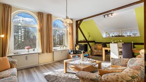 Ein Wohnzimmer mit Sofa, Couchtisch, Fernseher und einem Essbereich mit Stühlen und Tisch.