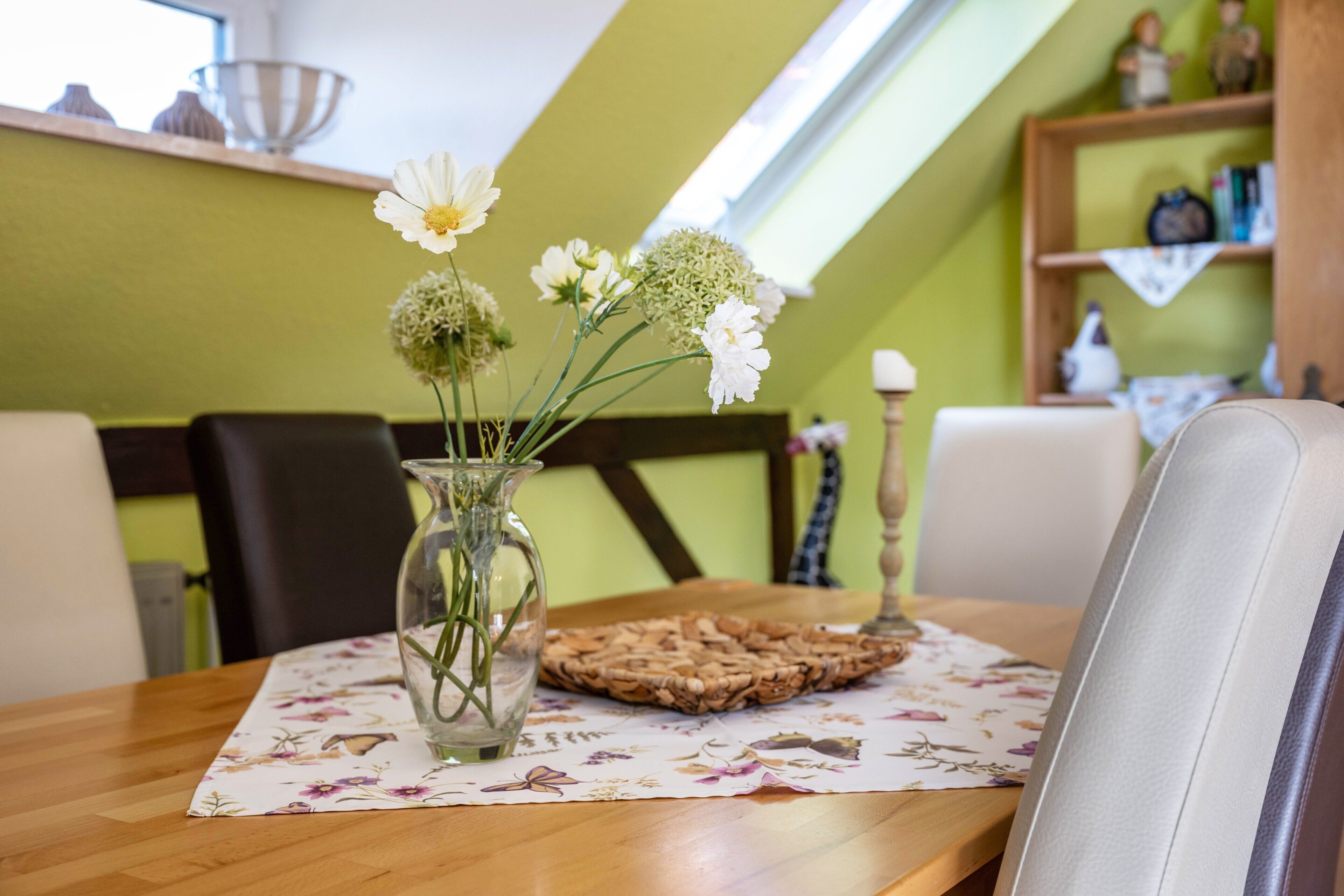 A dining table with a floral tablecloth, a clear vase with flowers, and a woven placemat.