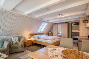 Um quarto de loft aconchegante com teto inclinado, uma cama, um espaço de estar com uma poltrona, uma mesinha e um pequeno espaço de cozinha.