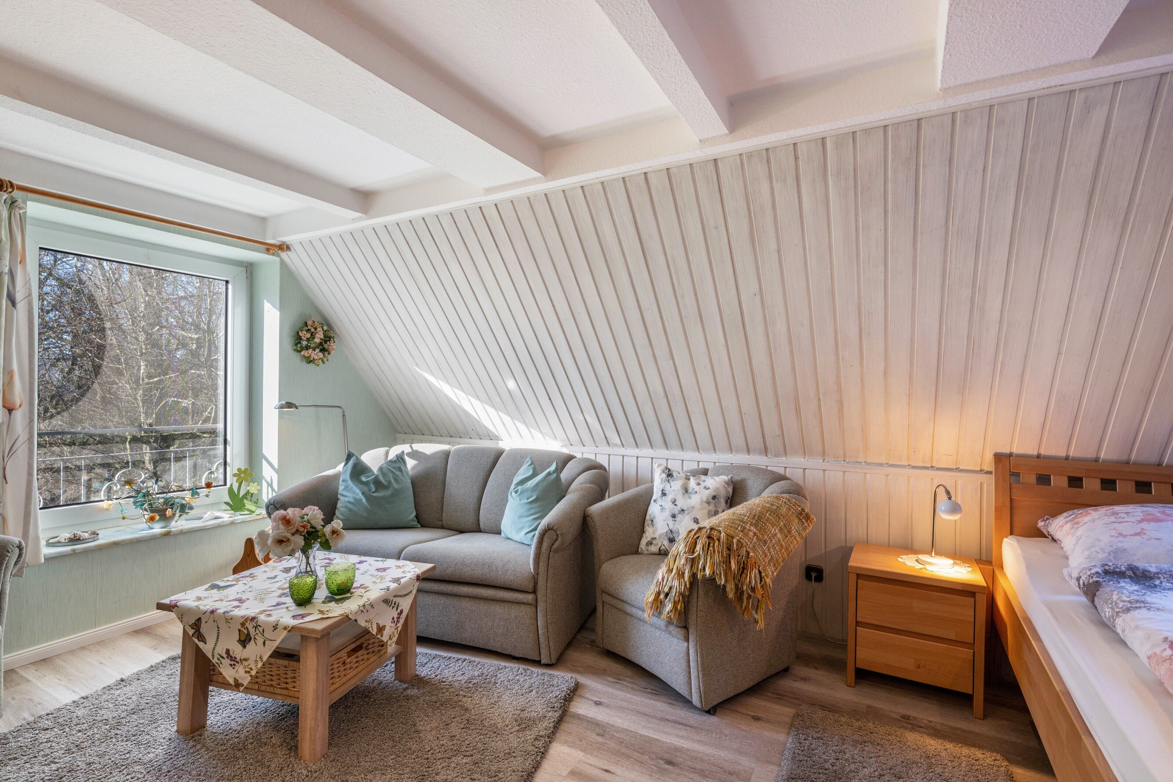 A cozy loft bedroom with a sloped ceiling, a sofa, a bedside table, a lamp, and a bed.