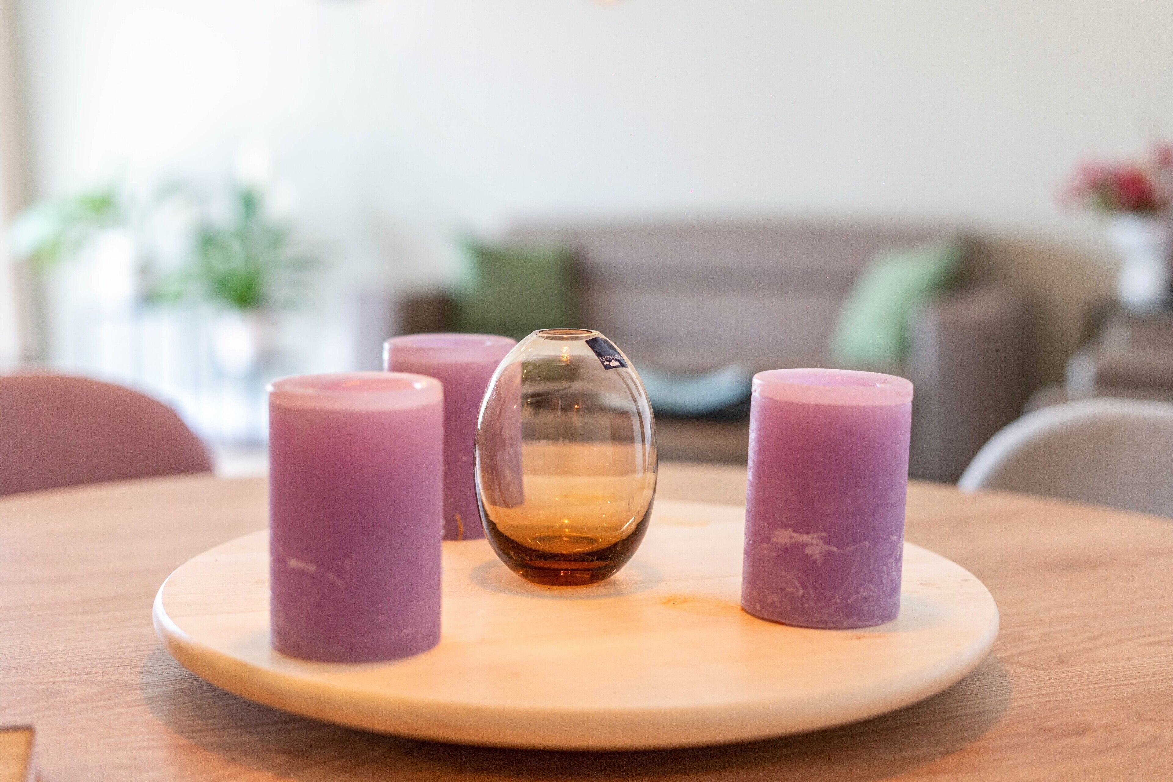 Una mesa redonda de madera con un florero de vidrio y tres velas moradas.