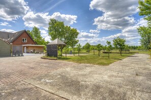 A residential property with a paved driveway, a garage, a small wooden structure, and a grassy area with trees.