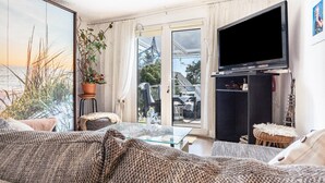Ein Wohnzimmer mit einer Couch, einem Glastisch, einem Fernseher und einer Zimmerpflanze.