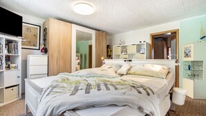 Ein Schlafzimmer mit Bett, Kleiderschrank, Regalen und einem Spiegel.
