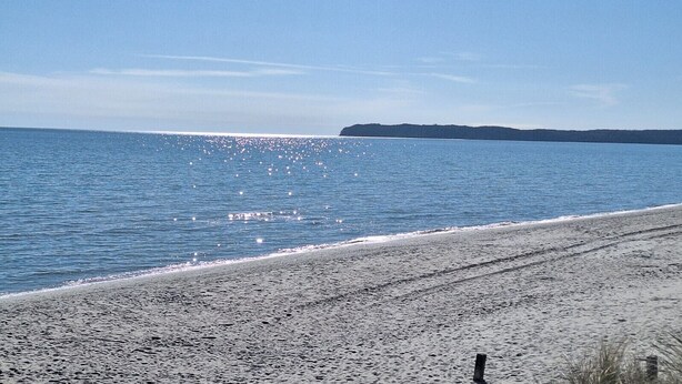 Ein Strand mit kiesigem Ufer und ruhigem Wasser, das das Sonnenlicht reflektiert.