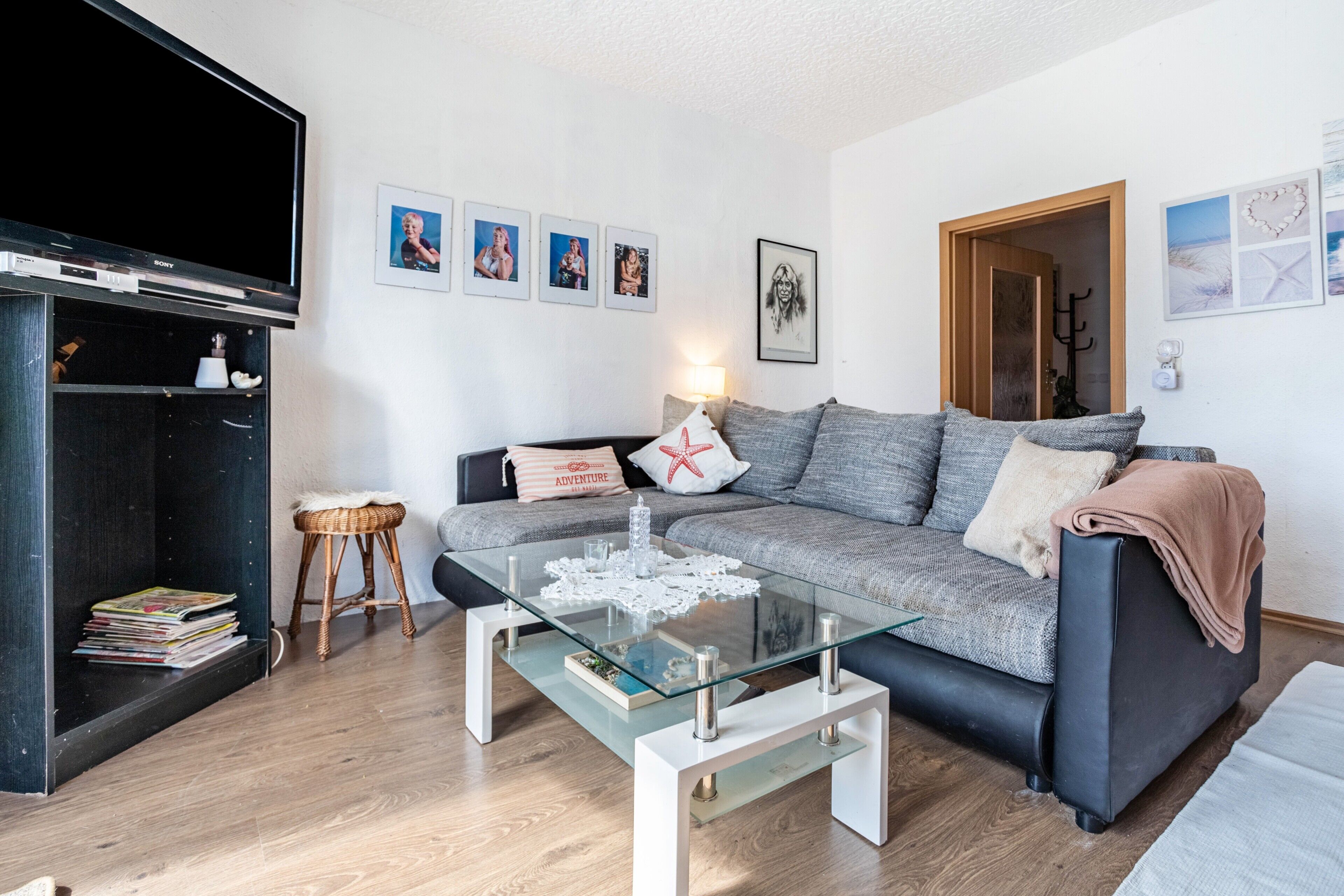 A living room with a glass coffee table, grey sofa, and a television.