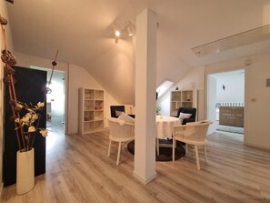 A spacious loft with a high ceiling, a dining area with a table and chairs, and a large window allowing natural light.