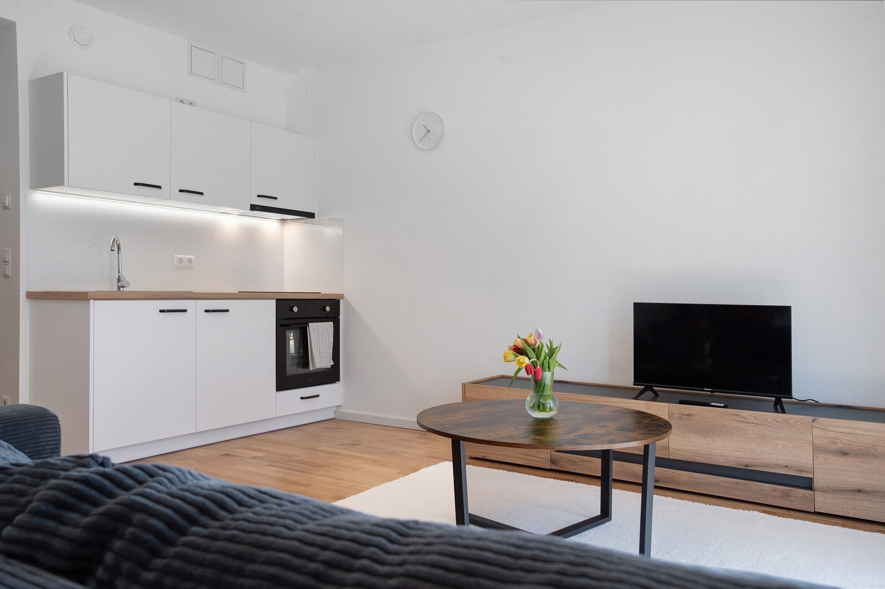 A modern kitchen with white cabinets, a built-in oven, and a wooden dining table with a vase of flowers.