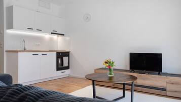 A modern kitchen with white cabinets, a built-in oven, and a wooden dining table with a vase of flowers.