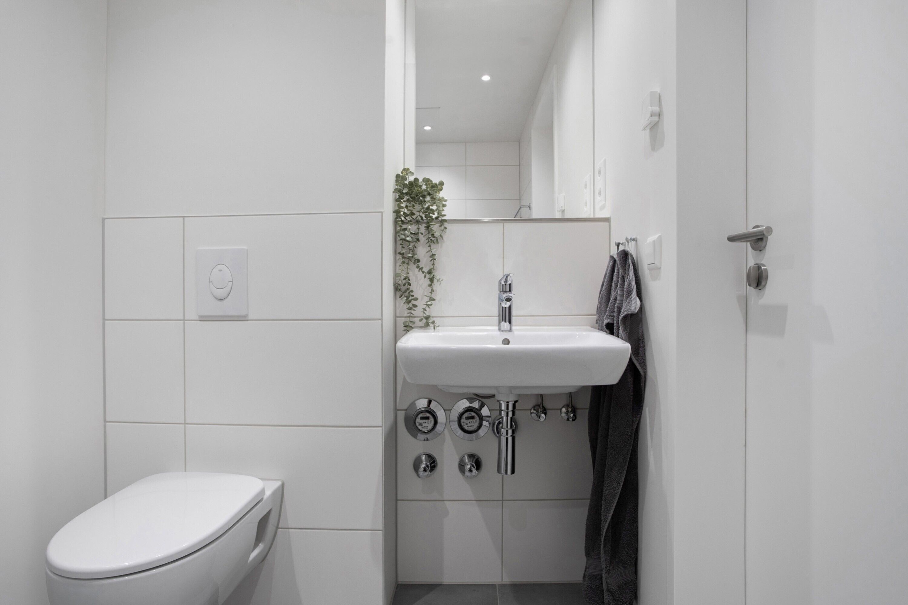 Un bagno moderno con il water bianco, un lavandino con uno specchio sopra e un asciugamano appeso al muro.